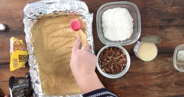 Crushed Graham cracker crumbs being spread out onto the buttered foil lined dish