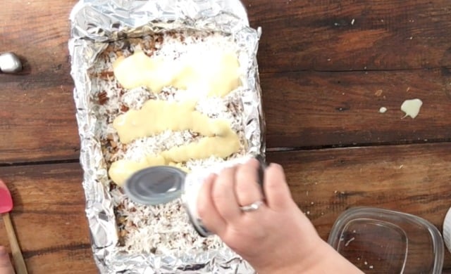 Pouring a can of sweetened condensed milk over the top of the other ingredients