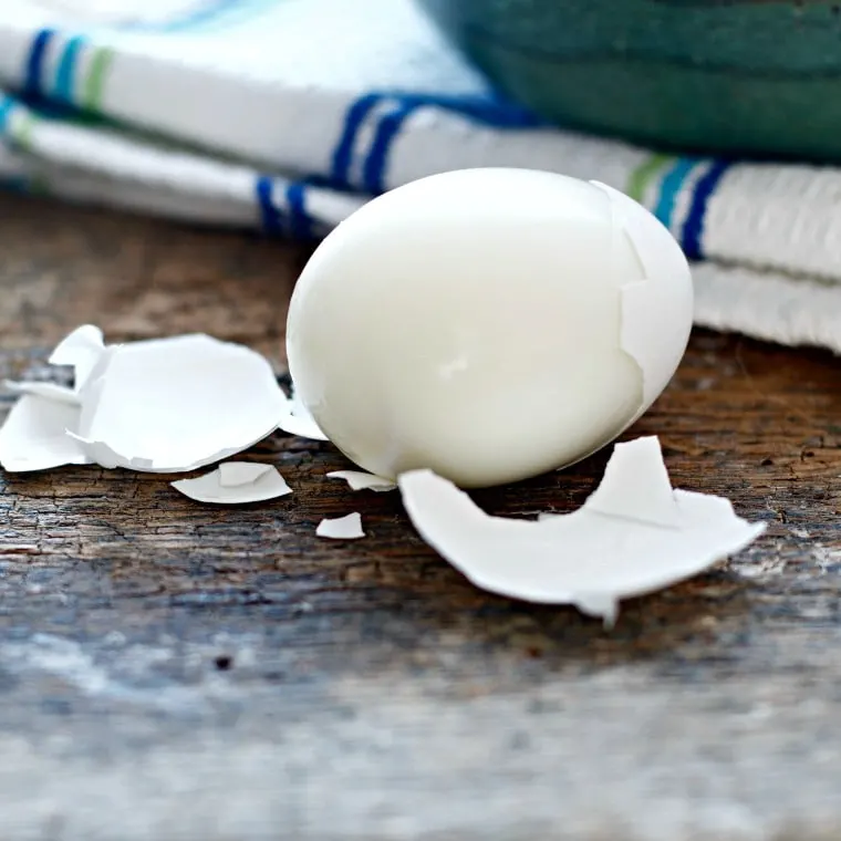 A hard boiled egg laying on a wooden table, blue and white towel in the background.