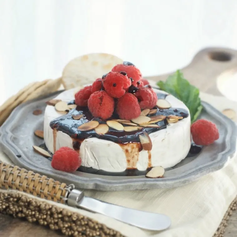 A side view of baked brie with sauce and raspberries on top.