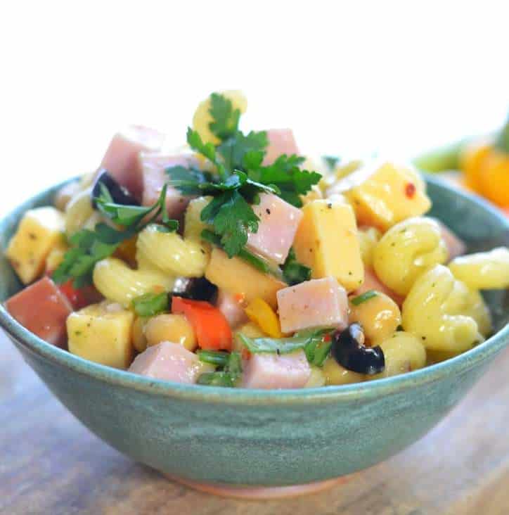 A side view of a green bowl of pasta salad showcasing the parsley, ham, cheese and noodles