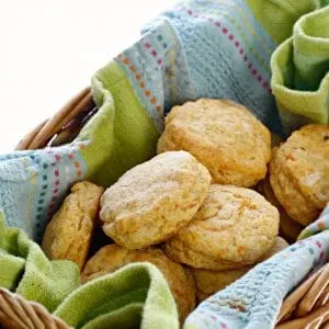 A photo of Southern Sweet Potato Biscuits in a basket with a blue and green kitchen towel