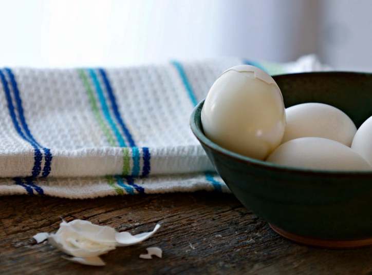 A bowl of eggs with one peeled one on top, towel in background.
