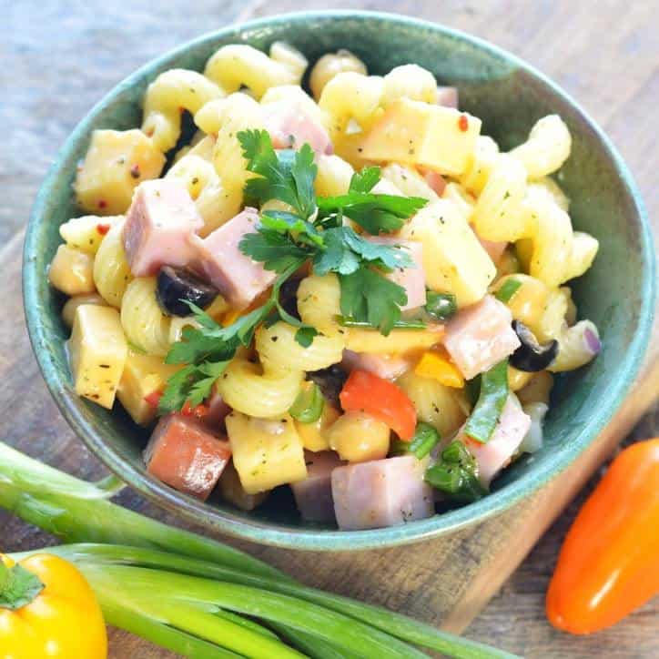 A close up overhead view of a green bowl of pasta salad with onion, pepper and ham.