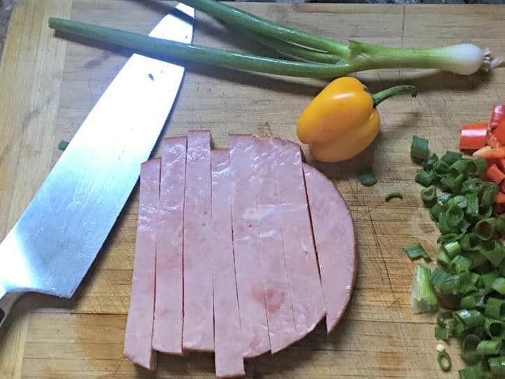 A photo of ham, a pepper, green onion on the cutting board with knife