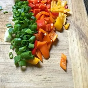 A photo of four colors of chopped peppers cut up on the cutting board - green, red, yellow and orange