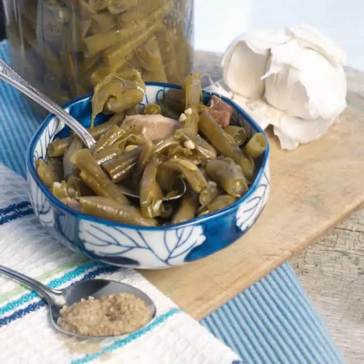 A photo of how to cook green beans in a blue bowl on a cutting board, garlic, sugar and beans in background