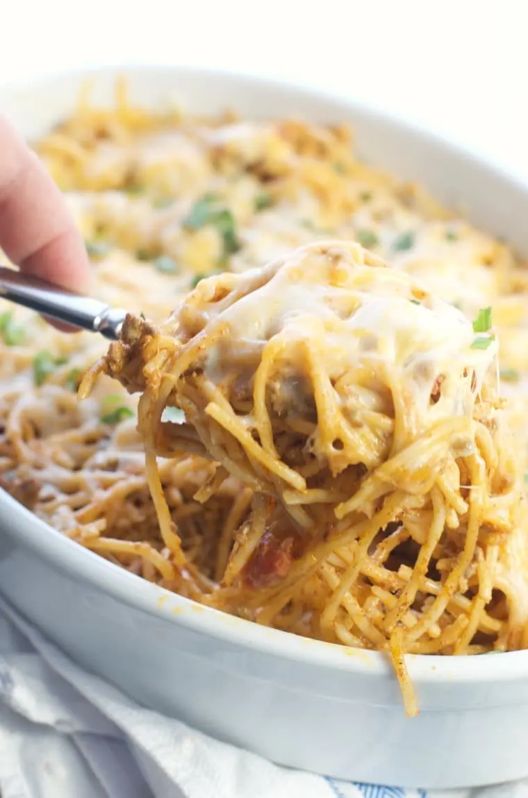 A spoonful of Amazing Baked Taco Spaghetti being scooped from the dish with cheese pulls