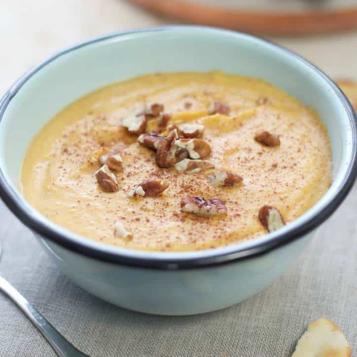 Blue bowl of roasted butternut squash soup with pecans crumbled on top.