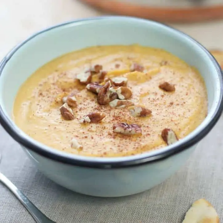 blue bowl with black rim of butternut squash soup, chopped pecans on top.