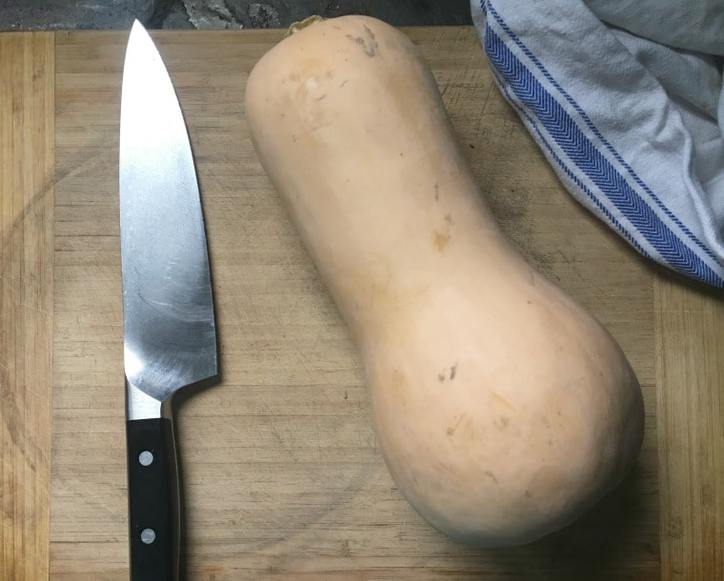 A photo of a butternut squash and a knife on a cutting board.