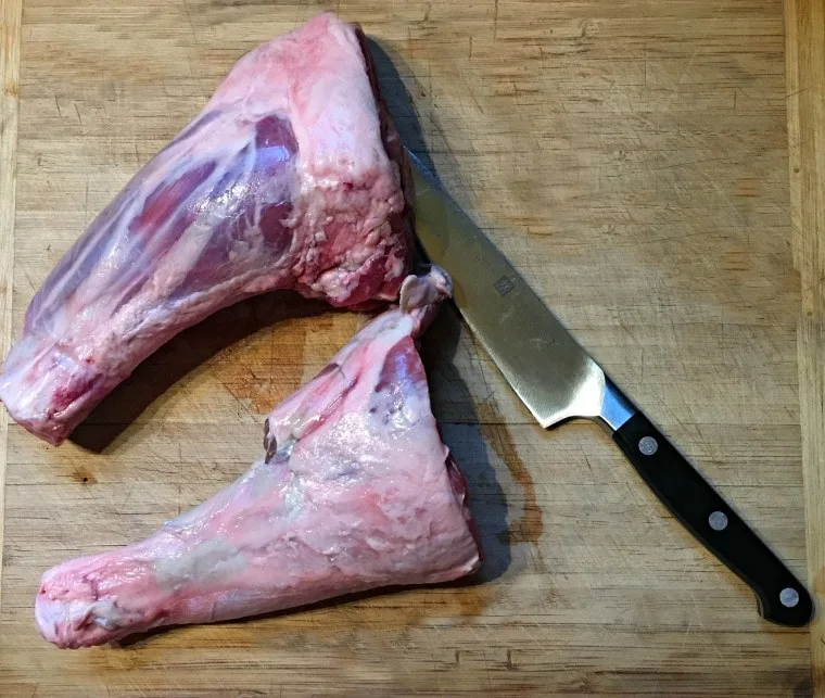 Two lamb shanks on cutting board with knife showing their silver skin