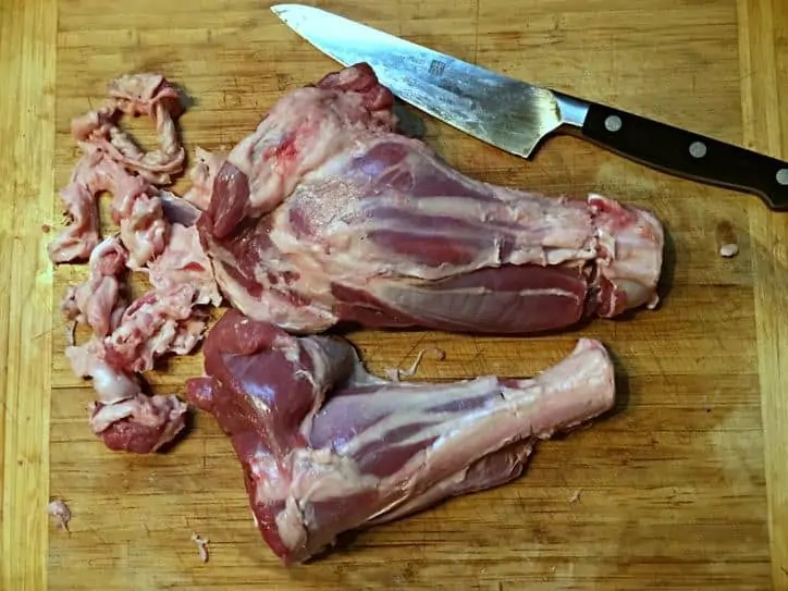 Lamb shanks on cutting board with knife with the fat removed, cut around small end.