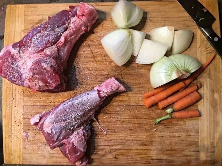 The meat, onions, carrots and knife on a cutting board