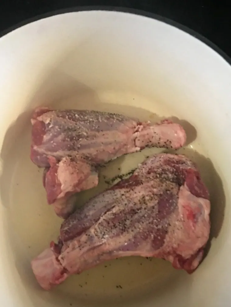 Salted and peppered prepared lamb shanks in dutch oven