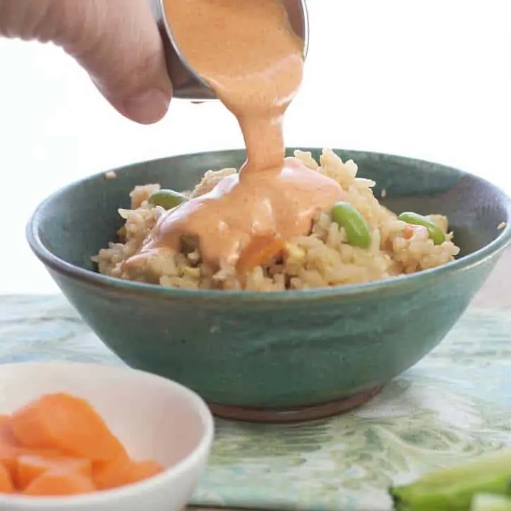 Shrimp Sauce being poured over a bowl of asian rice in a green bowl with green napkin under