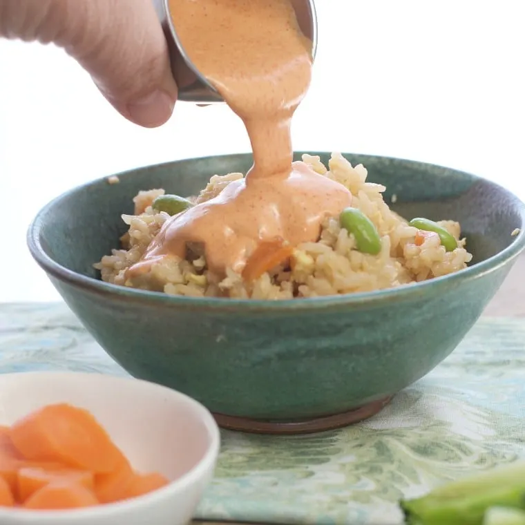 The being poured over a bowl of asian rice in a green bowl, napkin carrots in foreground.