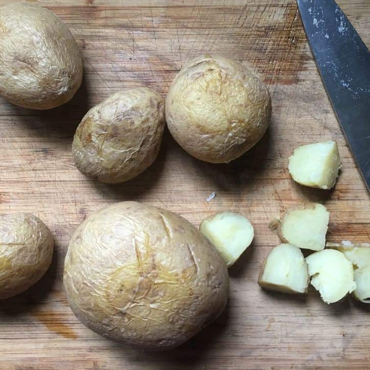 Potatoes on a cutting board with some cut into 2" pieces