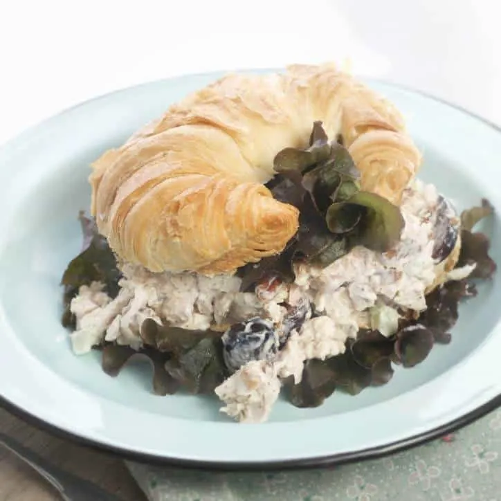 An image of How to Make Southern Style Chicken Salad with Rotisserie Chicken on a croissant with the chicken salad falling out the sides and lettuce poking out under the chicken salad