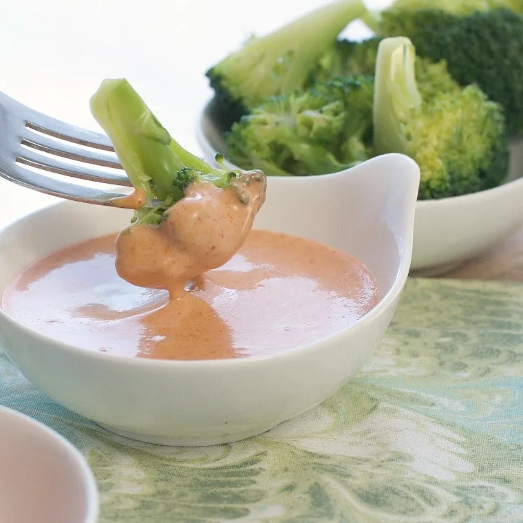 Small white bowl with pink japanese white sauce with broccoli being dipped in with fork