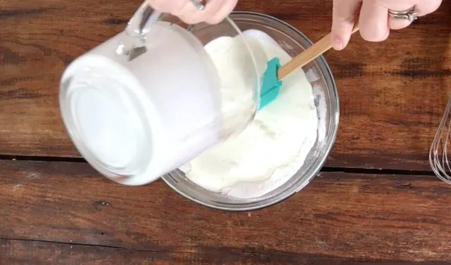 Pouring the heavy cream from a liquid measuring cup into the glass bowl of dry ingredients