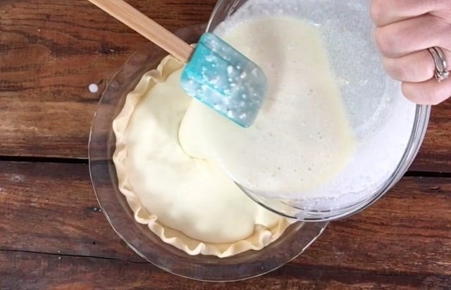 Pouring the glass bowl contents into the pie crust using a green spatula
