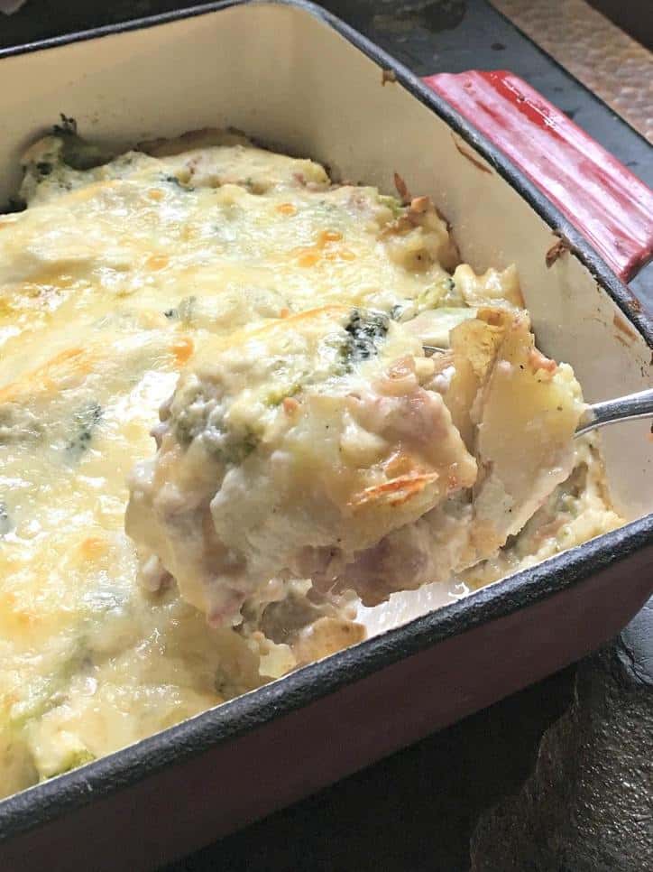 Red baking dish with spoon lifting up a bite of baked potato casserole