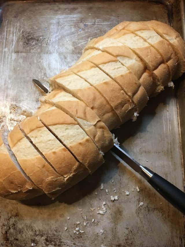 Loaf of Italian Bread sliced into 1 inch slices with knife and baking pan