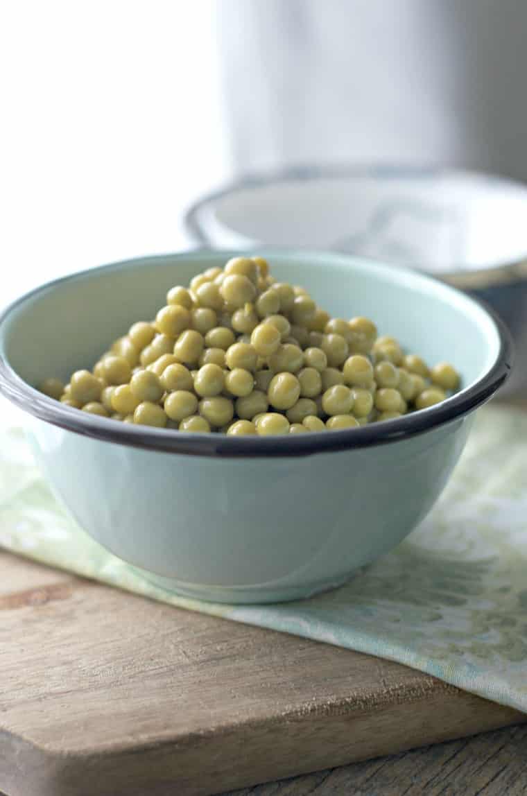 a blue bowl full of green peas sitting on cutting board