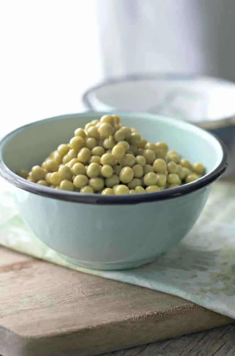 a blue bowl full of green peas sitting on cutting board