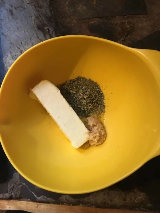 Stick of butter in a yellow bowl with herbs and garlic