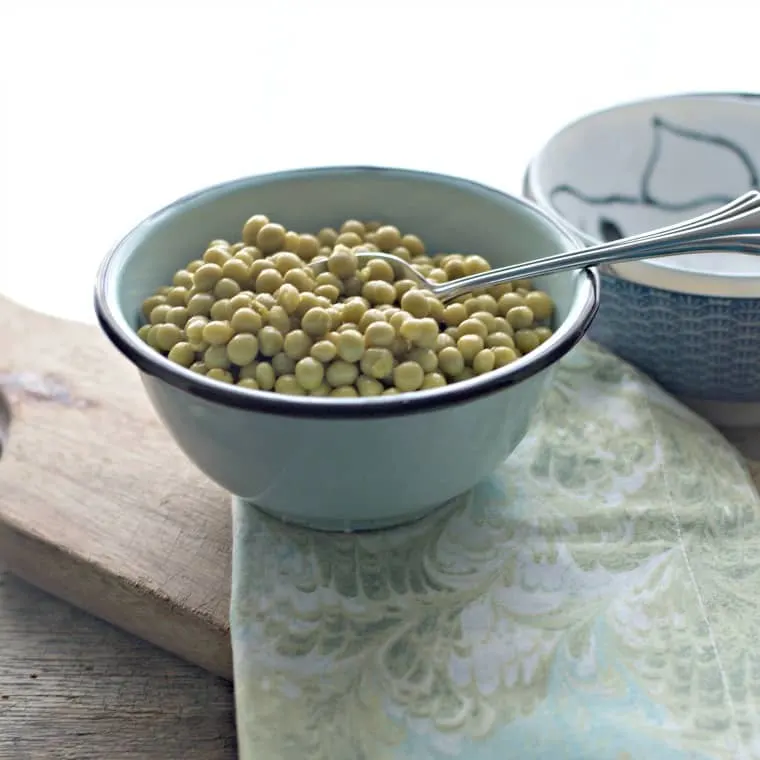 Blue bowl with spoon on cutting board. Frozen peas in the bowl.