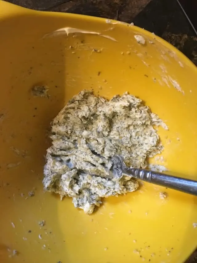 yellow bowl with butter, herbs and garlic smashed together with fork