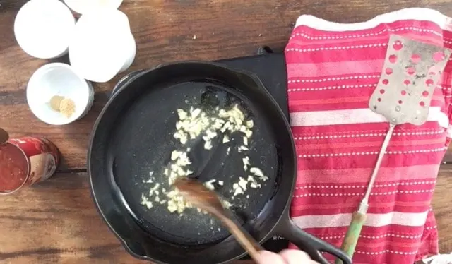 Garlic and onions browning in a cast iron skillet with red towel