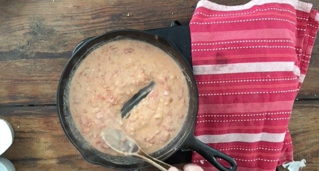 Wooden spoon stirring the tomato gravy in a cast iron skillet with red towel beside the pan