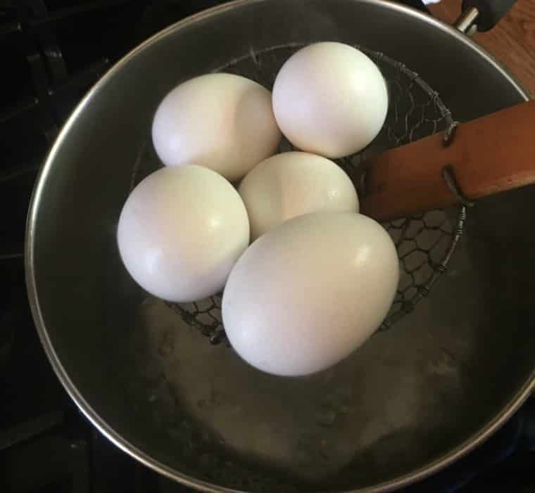 5 eggs sitting on a spider strainer over a stock pot of hot water. 