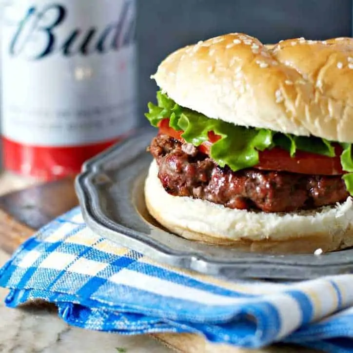 A close up of the Burger with a beer can in the back ground Biggest Baddest Best Hamburgers