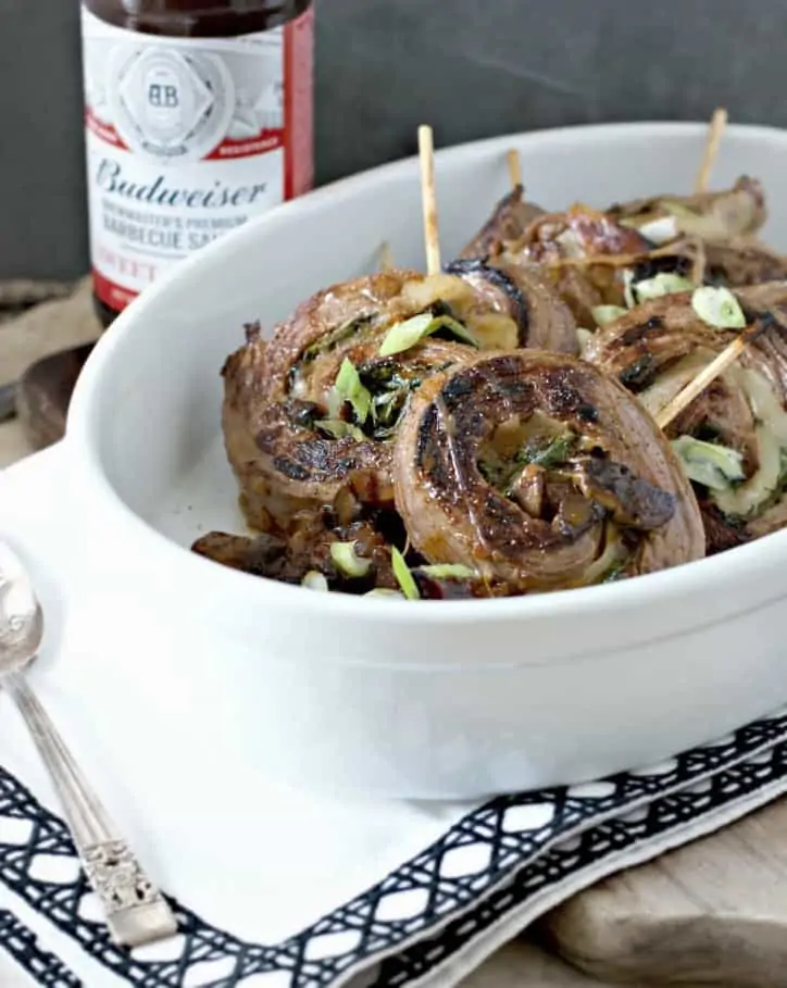 A farther away view of a barbecue flank steak roll ups with barbecue sauce in the back ground