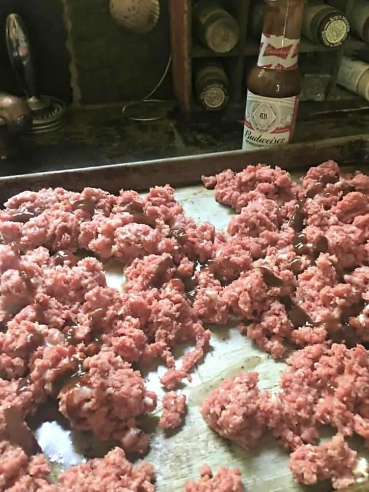 A photo of a baking sheet with meat, bacon fat and budweiser sauce drizzled over the top