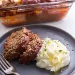 A slice of meatloaf with mashed potatoes and the pan in the background