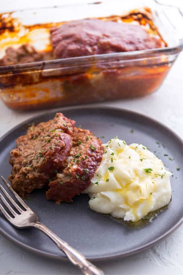 A slice of meatloaf with mashed potatoes and the pan in the background