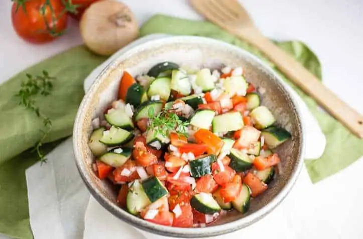 Pottery bowl with cucumber tomato salad with wooden bowl in background