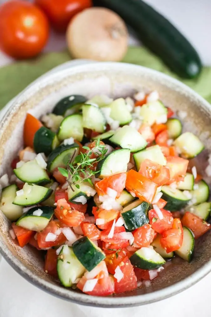 A close up view of cucumber tomato salad with veggies in background