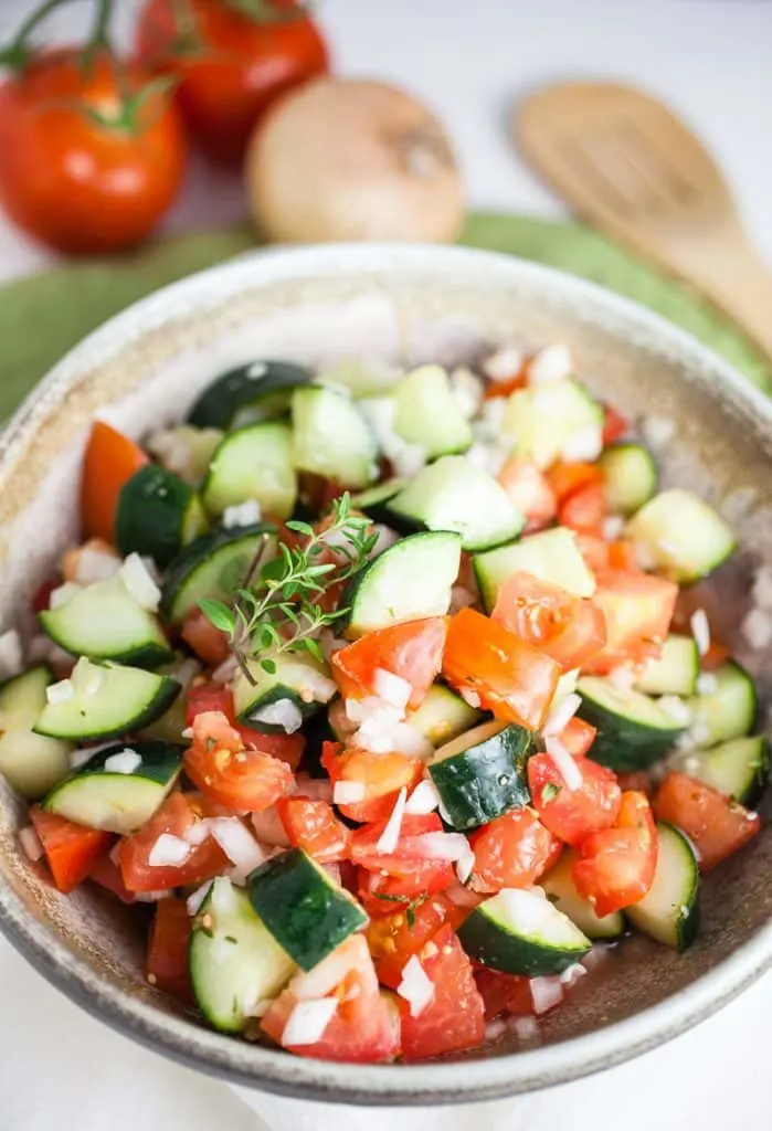 pottery bowl of cucumber tomato salad with wooden spoons in background
