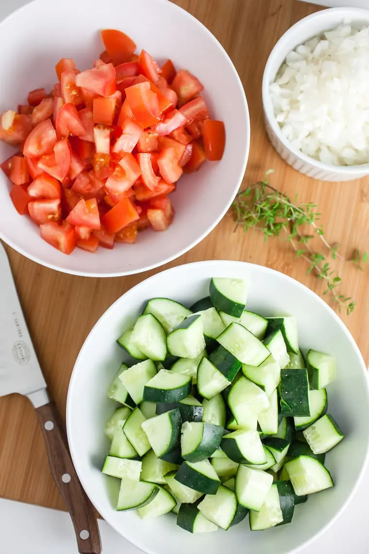 white bowls with chopped tomatoes and cucumbers on cutting board