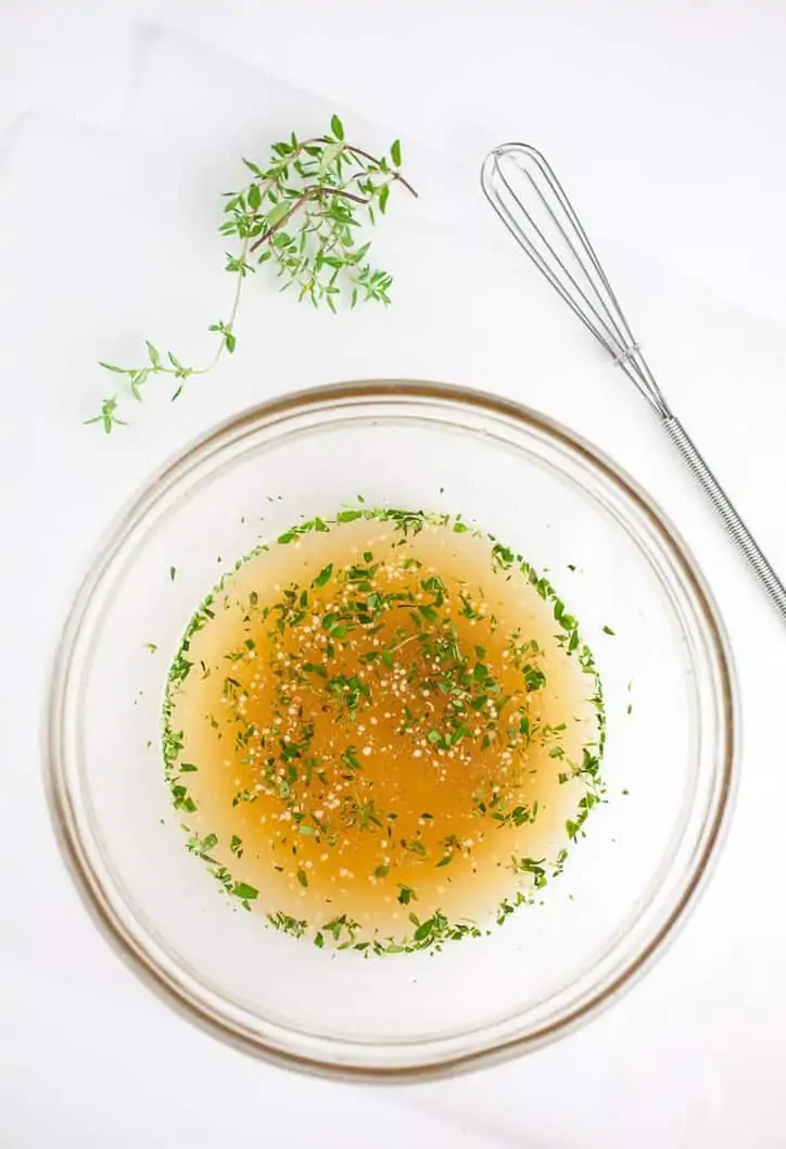 white bowl with gold rim full of dressing with whisk in background