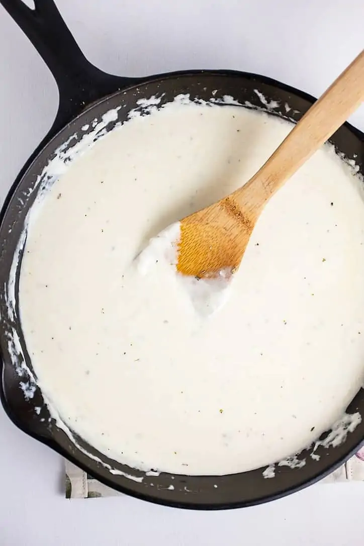 A photo of the alfredo sauce heated in a cast iron skillet with a wooden spoon