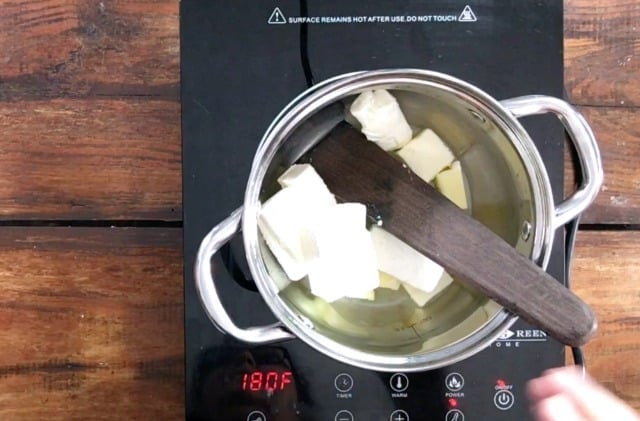 A saucepan on the stove with butter and cream cheese inside and a wooden spoon