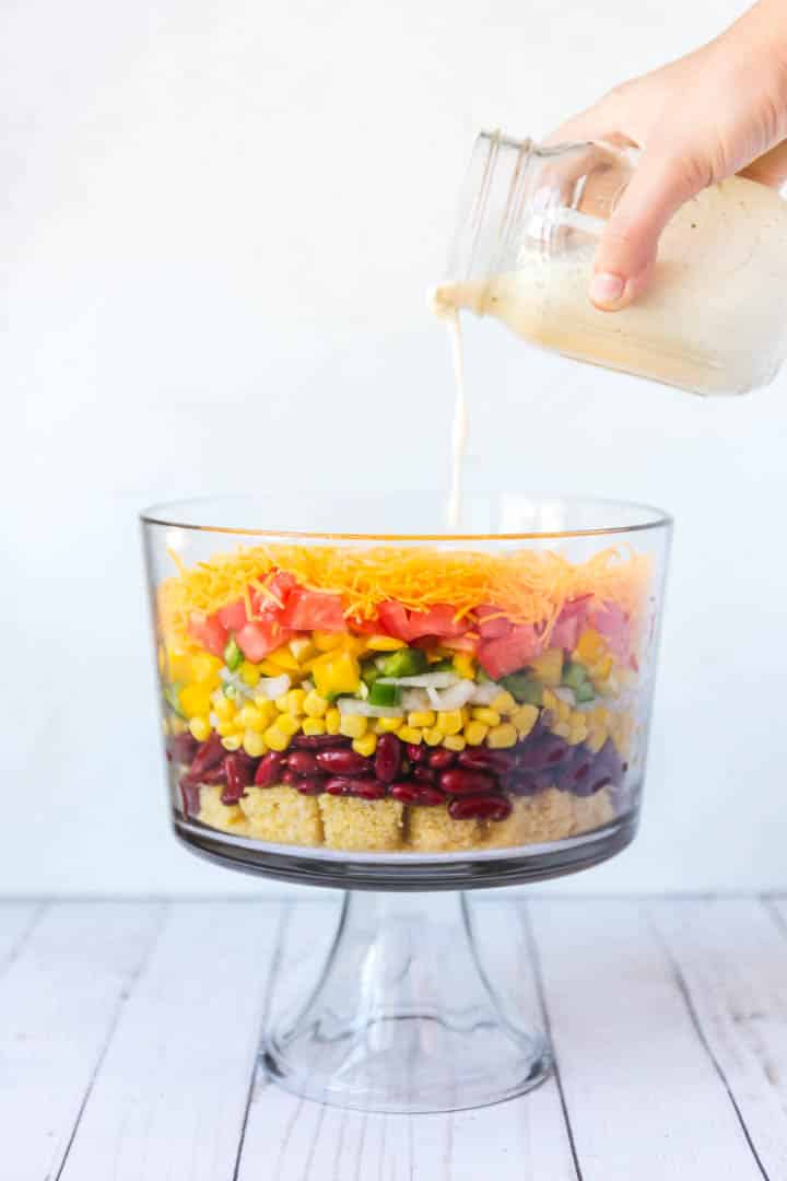 The ranch dressing being poured over the top of a colorful bowl of ingredients