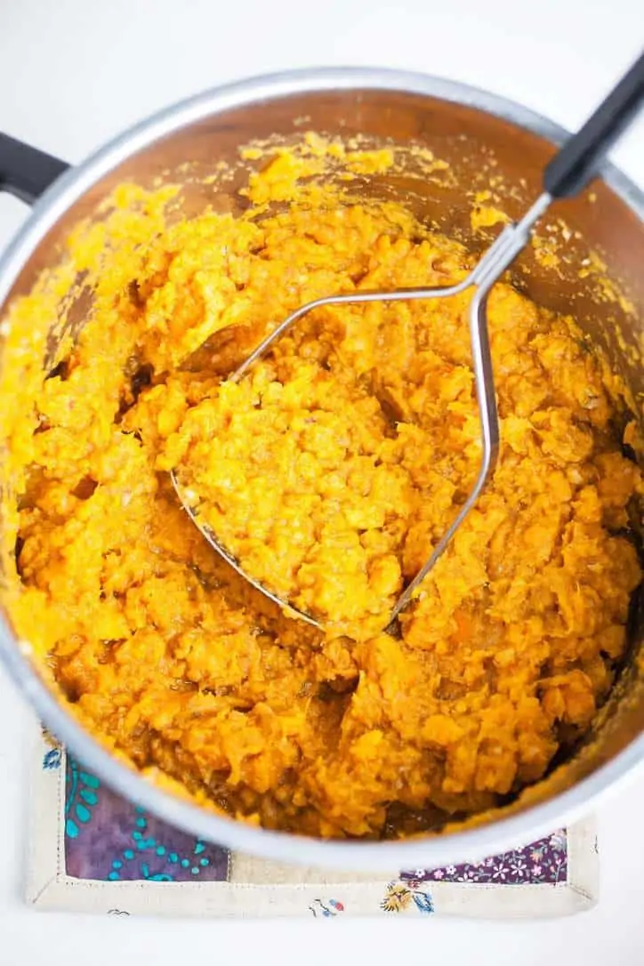 Mashed sweet potatoes in sliver pot with potato masher